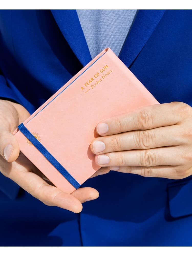 mėlynai apsirengęs vyras laiko rožinę užrašų knygutę rankose